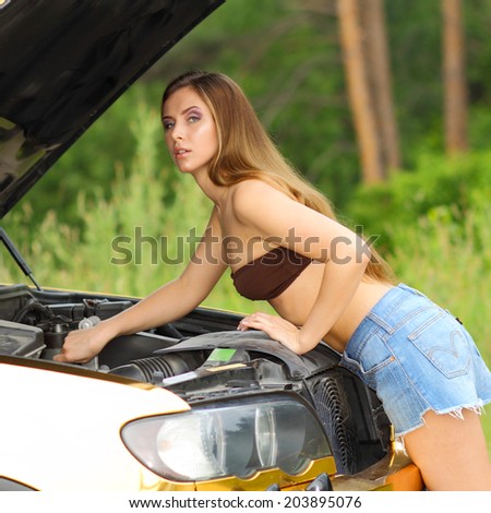 attractive girl in bikini looking under the hood of a car