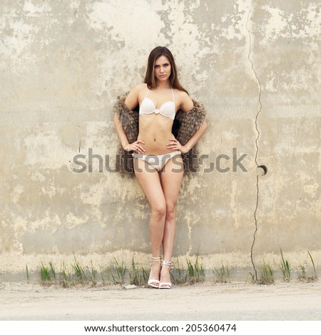 Beautiful slim girl in bikini posing on a background of textured old wall