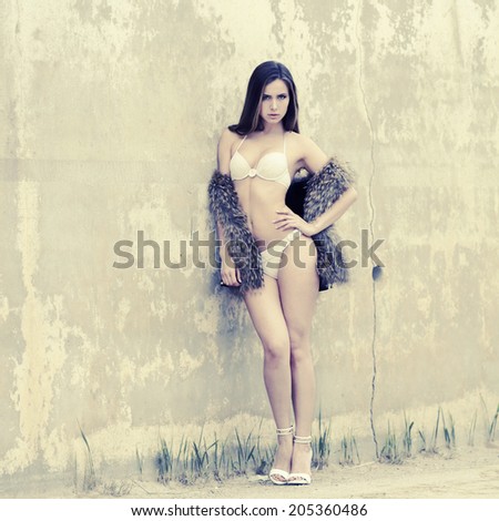 Beautiful slim girl in bikini posing on a background of textured old wall