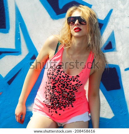 Modern fashion sexy girl in sunglasses posing near a blue wall graffiti