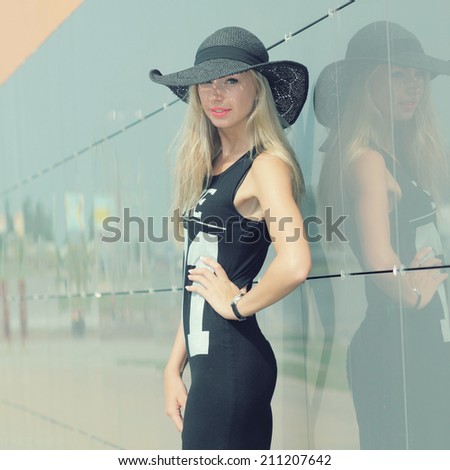 beautiful attractive trendy girl in long-skirted hat posing on the background wall mirror