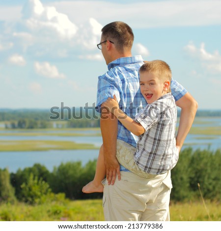 Father carrying his son piggyback. Blue sky on the background. Portrait of smiling father giving his son piggyback ride outdoors