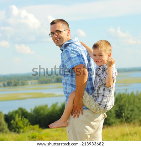 Father carrying his son piggyback. Blue sky on the background. Portrait of smiling father giving his son piggyback ride outdoors