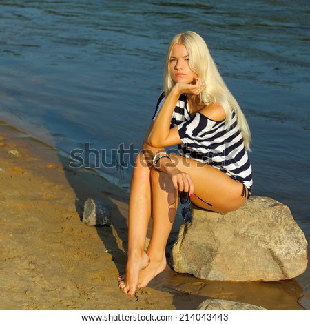 Fashionable beautiful blonde in a striped blouse enjoying on the beach near the water