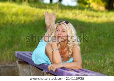 Beautiful mature blonde in a vintage dress posing on the bench. Portrait of positive elderly blonde woman