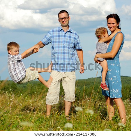 happy young family of four having fun on the top of a hill on a background of clouds