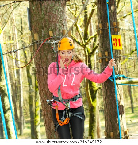 positive cheerful girl having fun doing tree climbing. Beautiful girl in the outfit climbing climbs over obstacles between trees