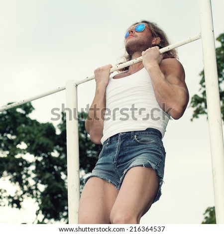 beautiful fitness model man doing exercise on bars outdoor.
