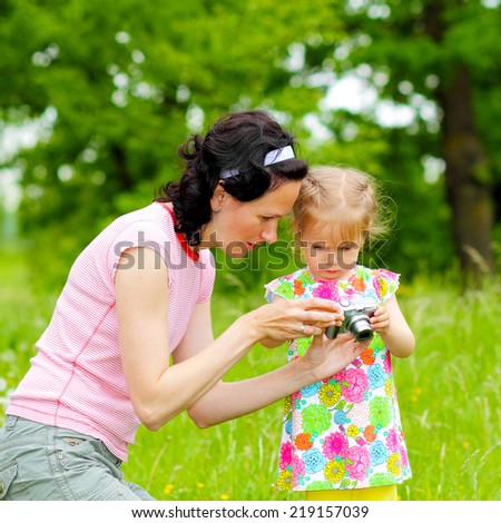 little girl child to learn to photograph with his mother in the meadow. little baby pictures with mom