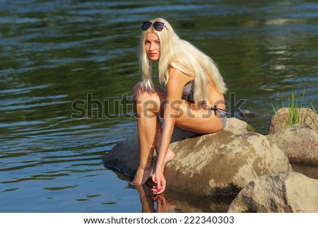 Attractive young blonde woman in a bikini sitting near the water