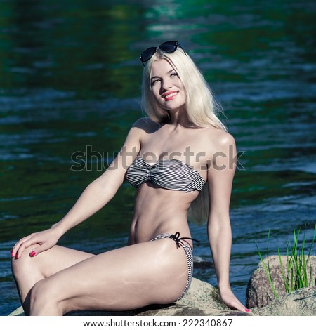 Attractive young blonde woman in a bikini sitting near the water. Pin up girl in vintage toning