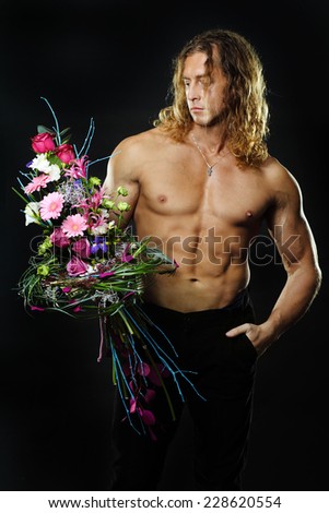 The long-haired male fitness model shirtless holding a bouquet of flowers. black background