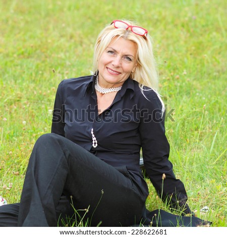 Beautiful elderly woman in black suit sitting on the grass. Beautiful older woman in vintage black suit sitting on the grass.