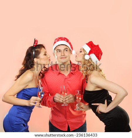 Two young attractive women kissing man. company enjoys Christmas.  Portrait of modern young people enjoying themselves at Christmas party.
