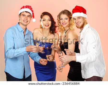 company enjoys Christmas.  Portrait of modern young people enjoying themselves at Christmas party. Company of friends in Santa caps holding flutes in hands