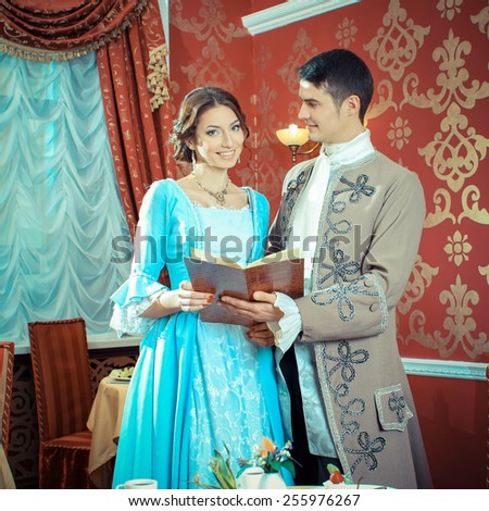 young man in a historic jacket and girl in vintage dress considering the menu in a restaurant. Elegant vintage couple in restaurant. Retro couple portrait. Romantic Beauty.Vintage Styled