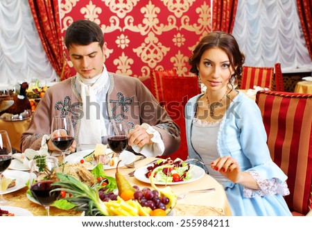 young man in a historic jacket and girl in vintage dress sitting at the richly laid table in a restaurant. Elegant vintage couple in restaurant. Retro couple portrait. Romantic Beauty.Vintage Styled