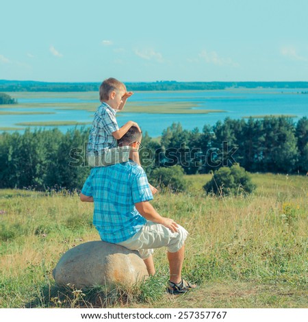 Dad and son happy on a hill in a landscape and open space. happy family against a landscape background. Outdoors on a background of sky and clouds. view from the back