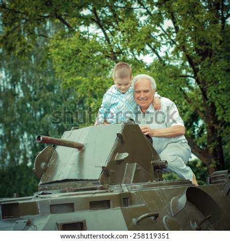 Grandfather and grandson explore military vintage historical transport. Grandfather and grandson at a military armored personnel carrier