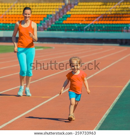 Mother & little daughter running around the stadium. Child runs away from mom at the stadium. Toned.