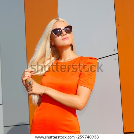 Portrait of trendy fashion girl in sunglasses and in orange dress on the background  of orange wall