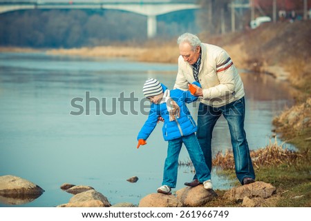Grandfather and grandson are crossing the river on the stones