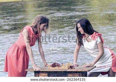 petite girls in a dress playing chess at a vintage table near the river. Vintage toning