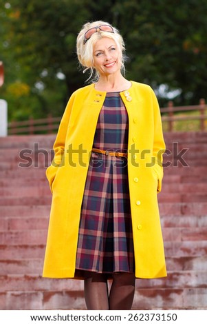 trendy Beautiful senior woman in a yellow coat walks in the park