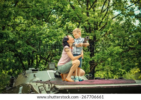 Mother with young son explore vintage military vehicles. family values on the background of a military tank