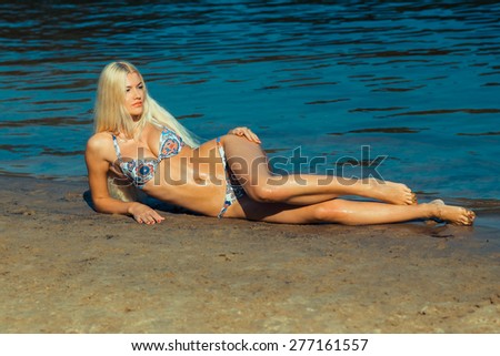 Beautiful young blond woman in a bikini on the beach near the sea