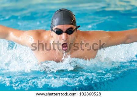 Man swimming butterfly strokes in competition wearing swimming goggles and cap