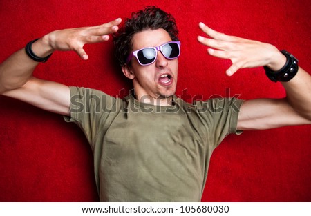 Young model making weird gestures on red background, wearing purple sunglasses. isolated