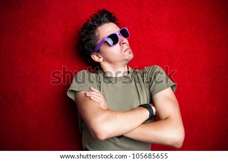 Young male model making strange face expressions on red background, wearing purple sunglasses isolated and staring
