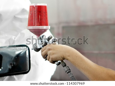 Worker using a red paint spray gun for painting a car