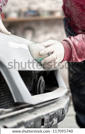 Mechanic preparing the body of a car for a paint job by applying the first layer of polish