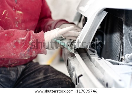 Auto mechanic preparing the front bumper of a car for painting