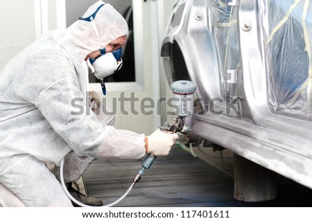 auto worker spraying grey paint on a car in an auto garage