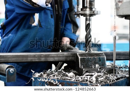 industrial technician working on a drilling machine - making a hole in a metal bar