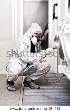 qualified worker spraying grey paint on a car in special painting booth