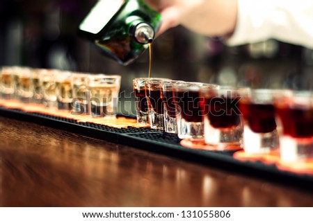 Bartender Pours Alcoholic Drink Into Small Glasses On Bar