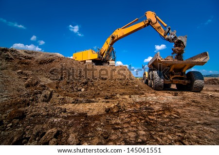 Industrial excavator loading soil material from highway construction site into a dumper truck