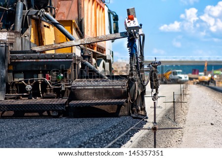 pavement machine laying fresh asphalt or bitumen on top of the gravel base during highway construction