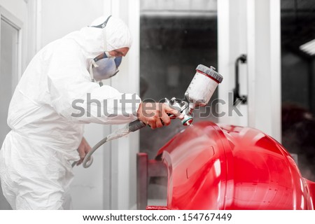 Engineer painting a red part of car with spray gun in special booth