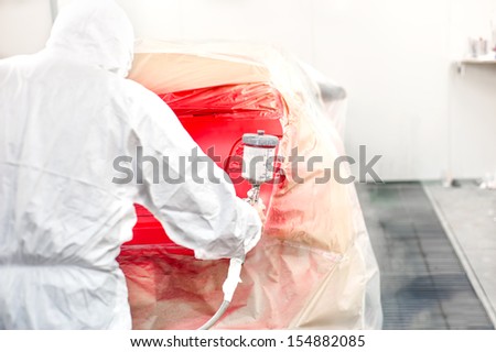 Automotive industry - car painter painting a red car in special booth wearing a white costume