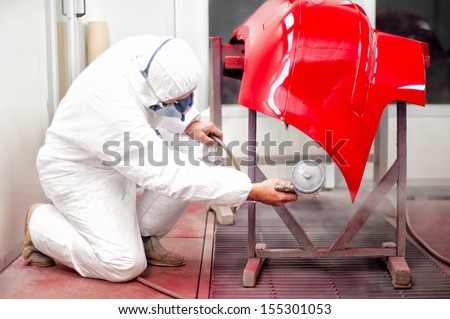 Auto mechanic painting with spray gun bumper of car in special booth