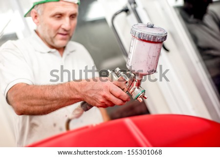 Close-up of spray gun and airbrush painting a red car