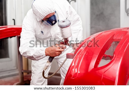 Painter working and painting a red car in paint garage