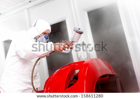 Detail of automotive engineer, mechanic painting a red bumper of a car in workshop