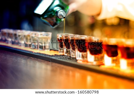 Bartender pouring strong alcoholic drink into small glasses on bar, shots