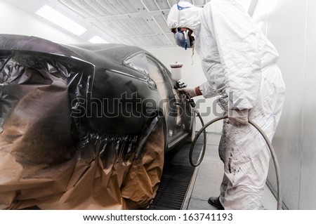 worker painting a car in a special painting box, wearing a white costume and protection gear
